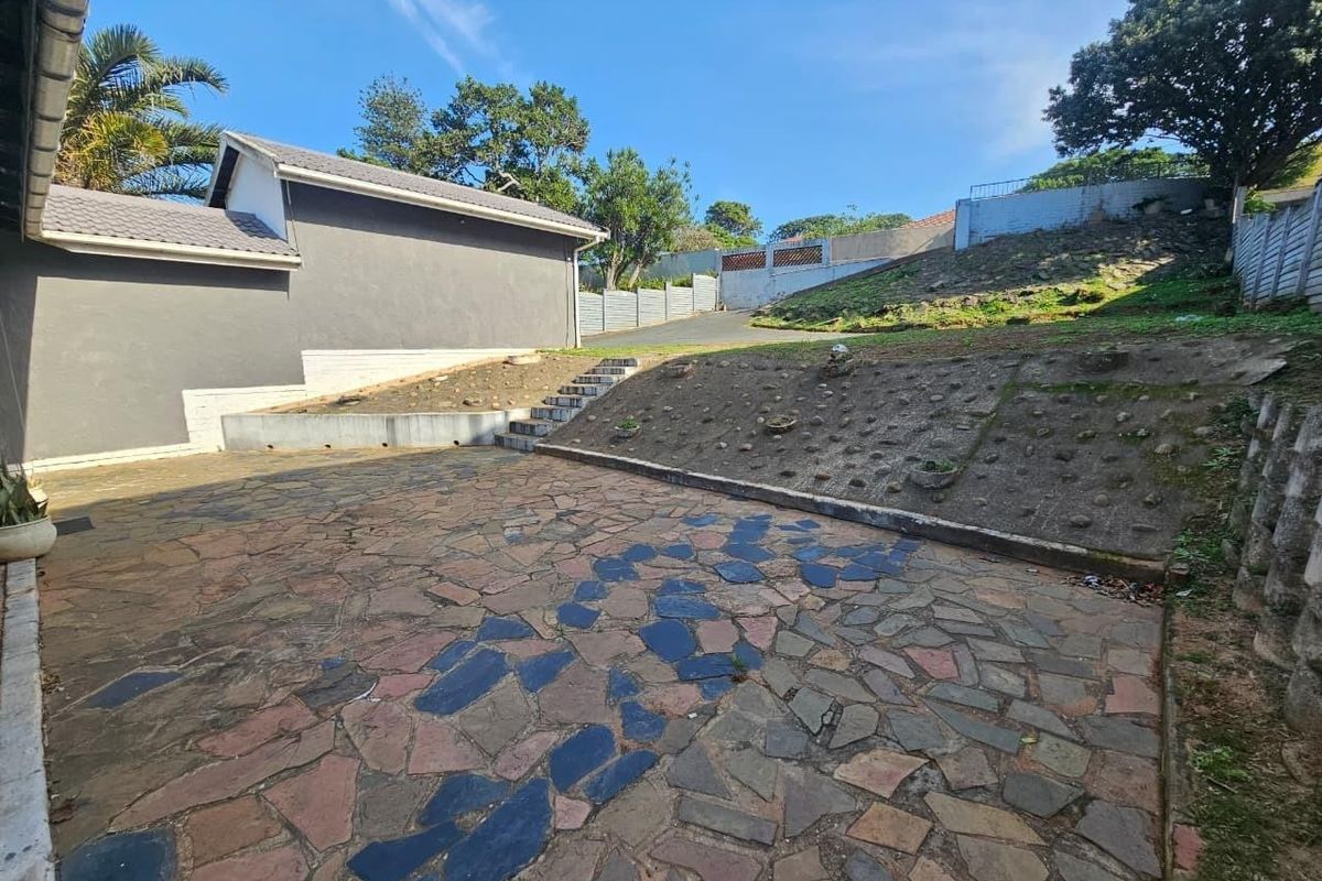 Rear exterior area featuring a stone paved patio, concrete stairs, and a tiered retaining wall structure in need of landscaping and maintenance.