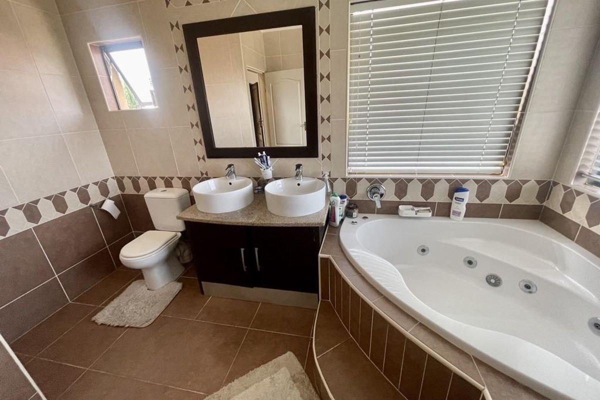 A spacious bathroom featuring a corner jetted tub, dual vanity with vessel sinks, and tiled flooring with decorative border accents.