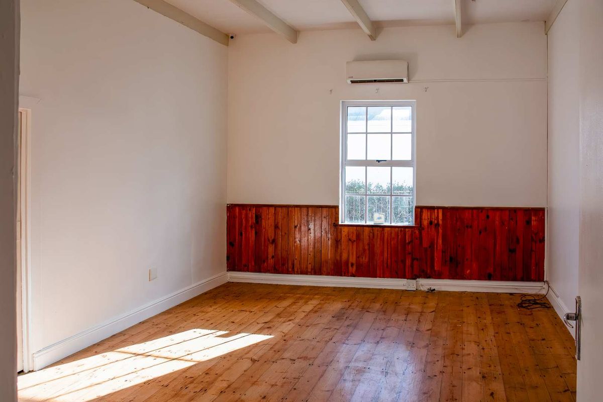 An empty bedroom featuring polished timber flooring, classic timber wall paneling, exposed ceiling beams, and a wall-mounted air conditioning unit.
