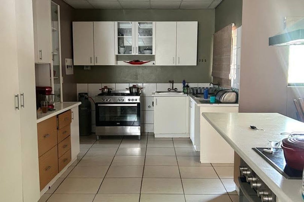 A functional kitchen featuring white cabinetry, a built-in oven with hob, tiled flooring, and a breakfast counter.
