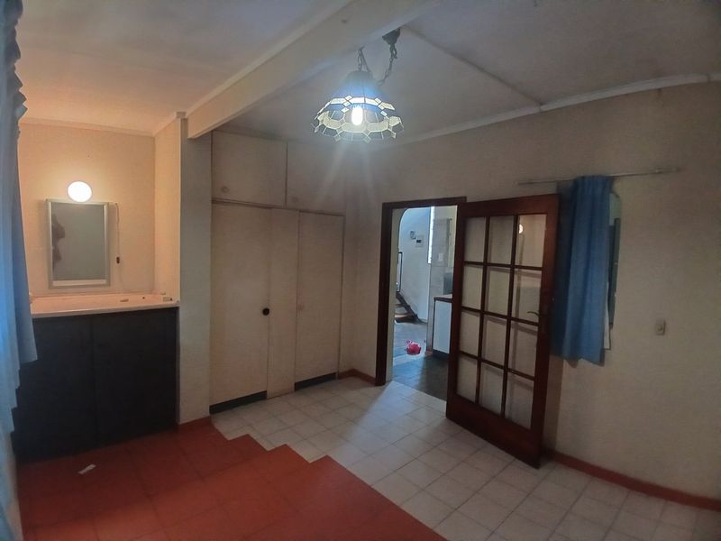 A spacious bedroom featuring built-in cupboards, a vanity basin, and tiled flooring, offering a functional layout with direct access to the hallway.