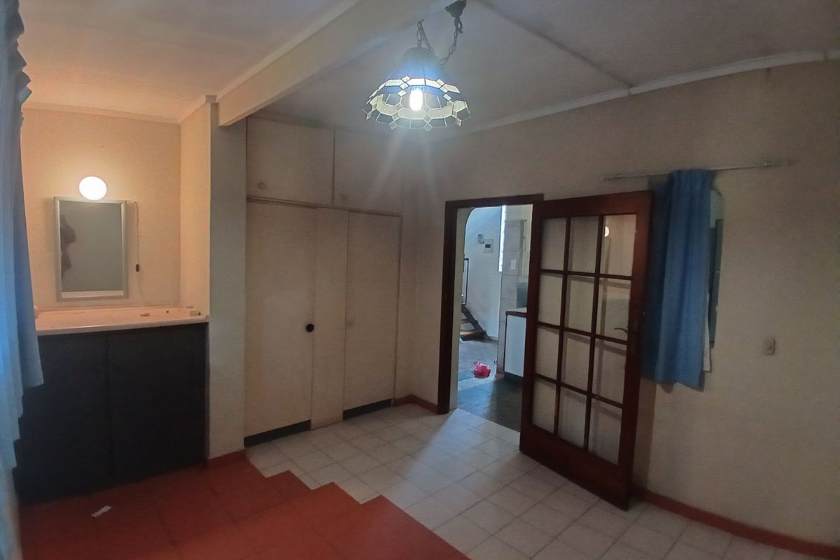 A spacious bedroom featuring built-in cupboards, a vanity basin, and tiled flooring, offering a functional layout with direct access to the hallway.