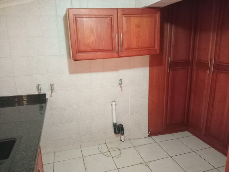 A functional laundry area featuring built-in wooden cabinetry, granite countertops, and tiled finishes, providing a practical space for utility and washing appliances.
