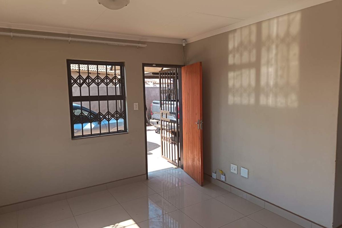 A bright, empty living area featuring neutral wall tones, tiled flooring, and secure access points with fitted security gates and window bars.