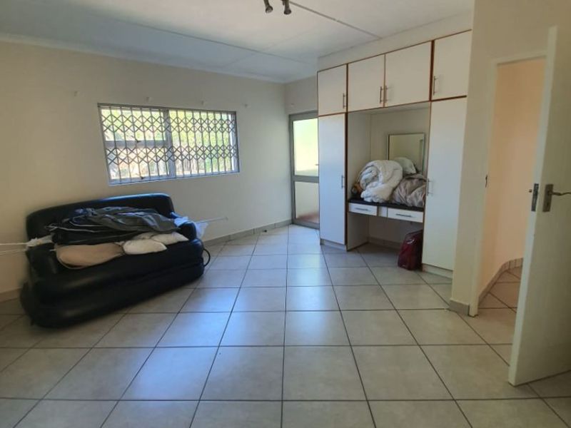 A bedroom featuring tiled flooring, built-in cupboards with a vanity area, and a window fitted with a security gate.