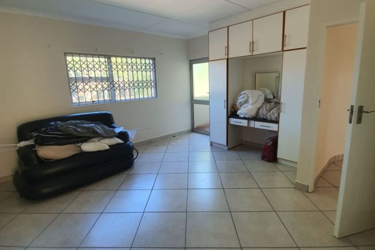 A bedroom featuring tiled flooring, built-in cupboards with a vanity area, and a window fitted with a security gate.
