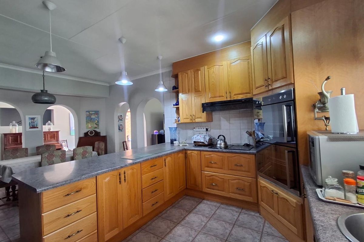 A functional kitchen featuring traditional wooden cabinetry, built-in oven and hob, tiled flooring, and an open-plan layout connecting to the dining area.
