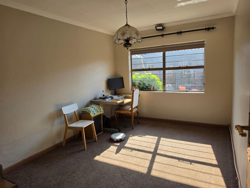 A bedroom featuring carpet flooring, a window with security bars, and a pendant light fixture, offering a functional space with potential for updates.