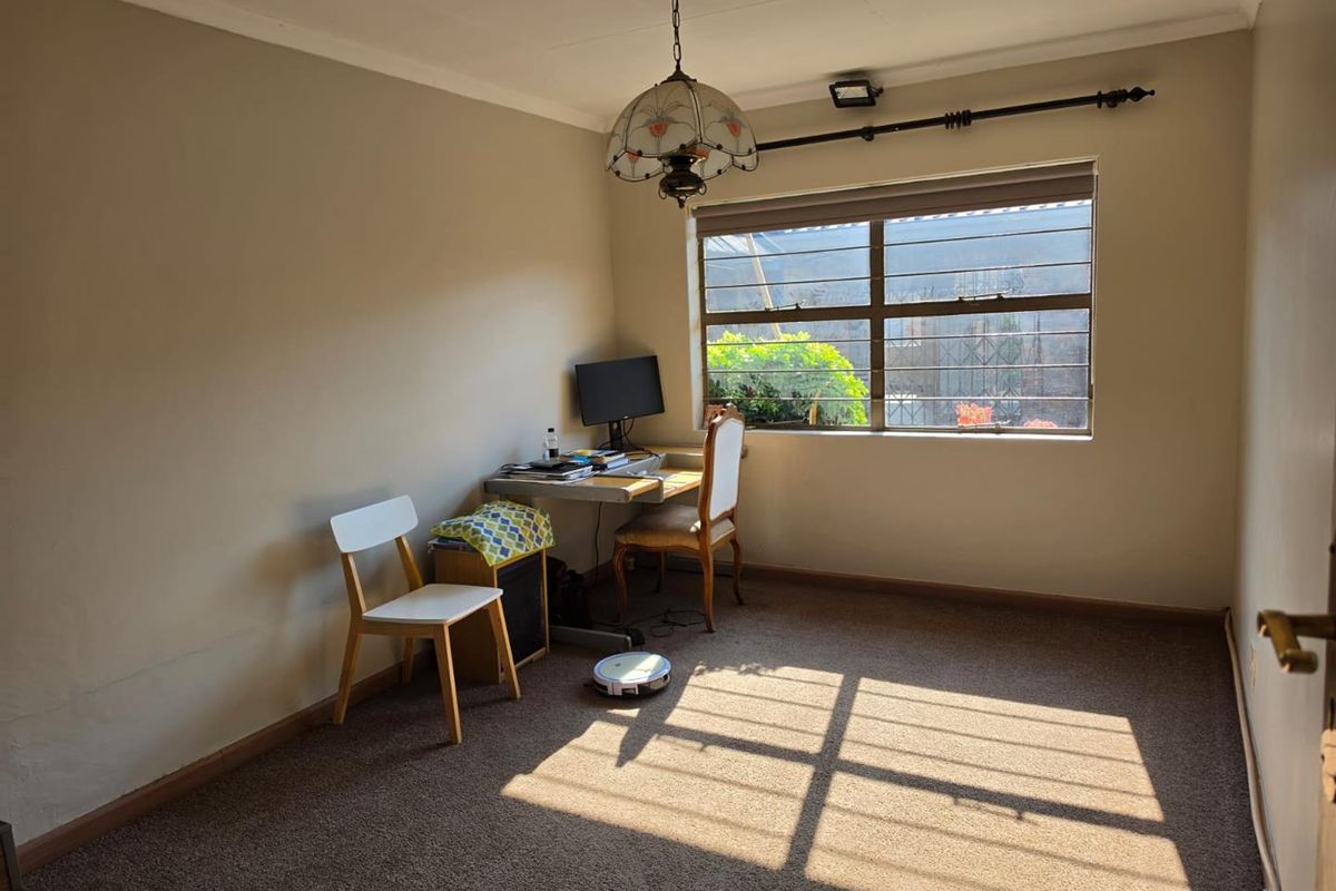 A bedroom featuring carpet flooring, a window with security bars, and a pendant light fixture, offering a functional space with potential for updates.
