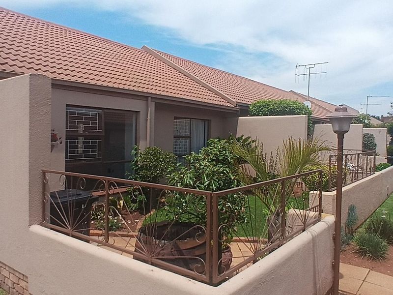 Rear view of a townhouse complex featuring a private garden area, paved walkways, and secure sliding door access.
