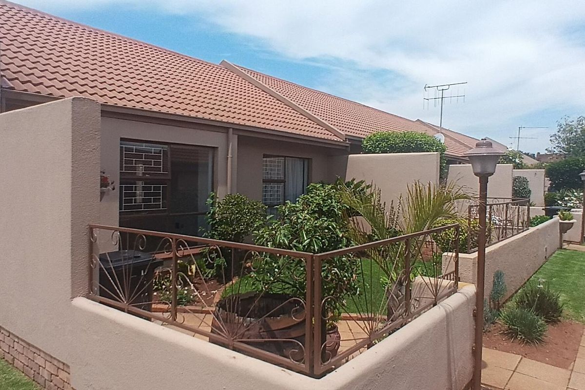 Rear view of a townhouse complex featuring a private garden area, paved walkways, and secure sliding door access.