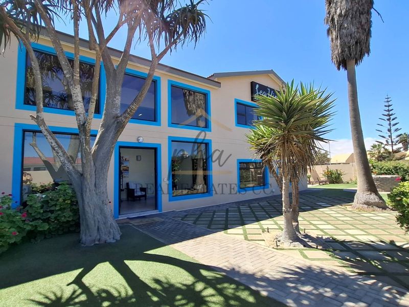 Front exterior view of the guest house featuring a paved driveway, landscaped garden, and large windows with blue trim.