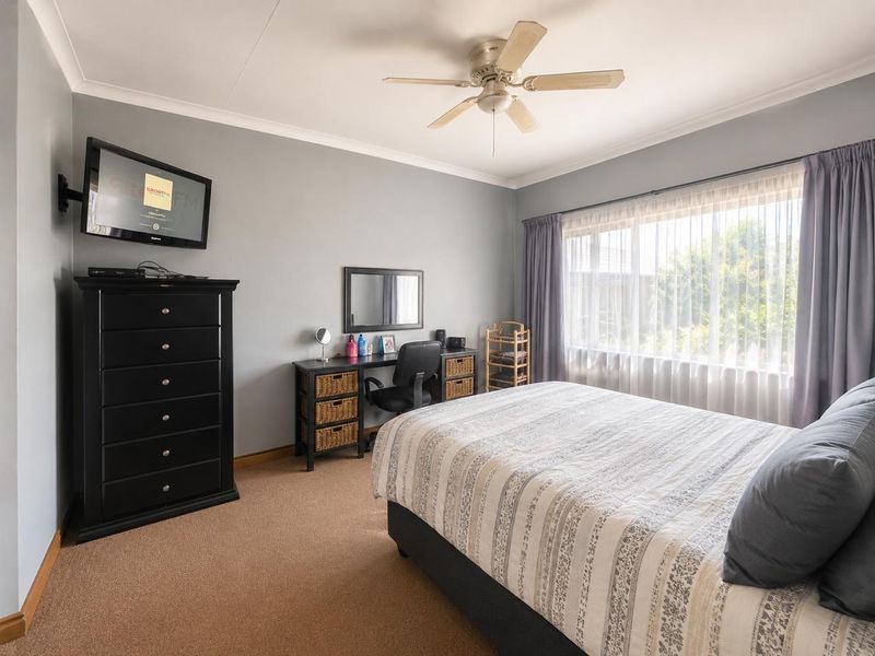 A well-maintained bedroom featuring neutral grey walls, carpeted flooring, and a ceiling fan, offering a comfortable and functional living space.