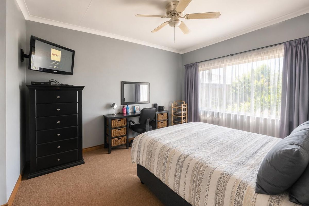 A well-maintained bedroom featuring neutral grey walls, carpeted flooring, and a ceiling fan, offering a comfortable and functional living space.