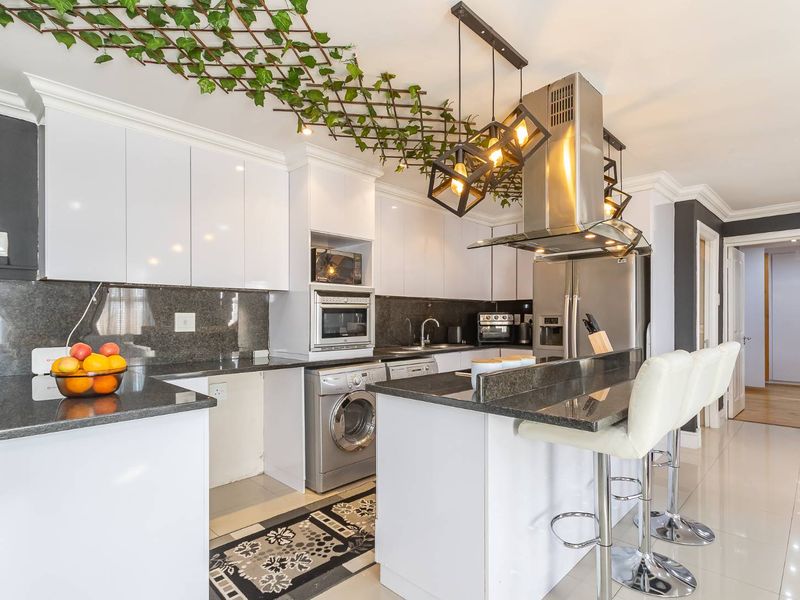Modern kitchen featuring sleek white cabinetry, dark granite countertops, a breakfast bar, and integrated stainless steel appliances, including an extractor fan and microwave.