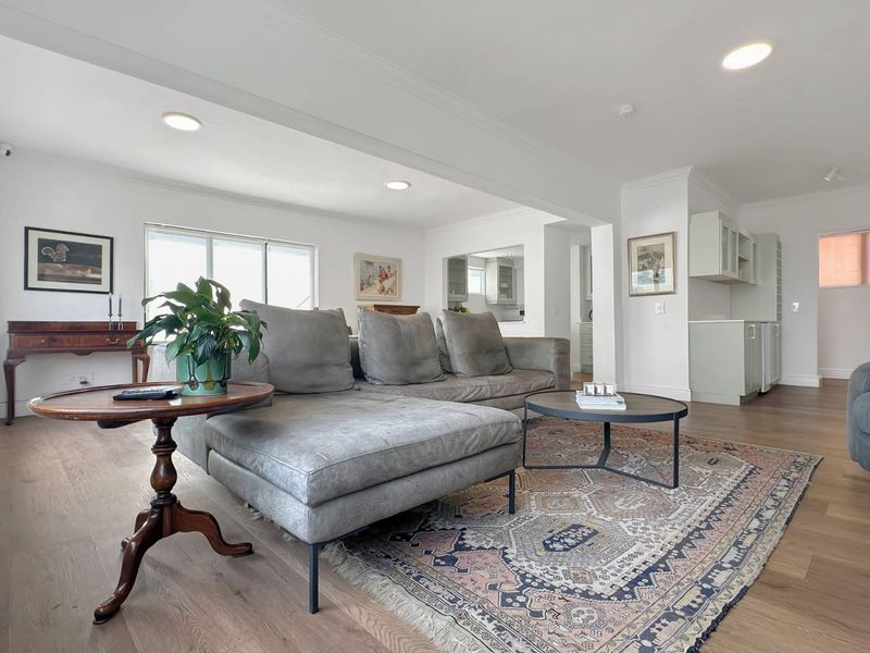 Spacious open-plan living area featuring light timber flooring, recessed downlighting, and seamless flow into the adjacent kitchen space.