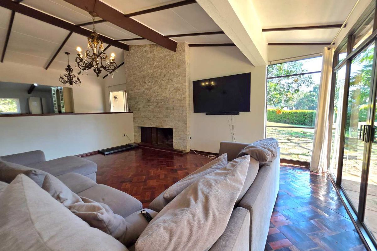 Spacious living room featuring exposed timber ceiling beams, a prominent stone-clad fireplace, and classic parquet flooring with large glass doors opening to the garden.