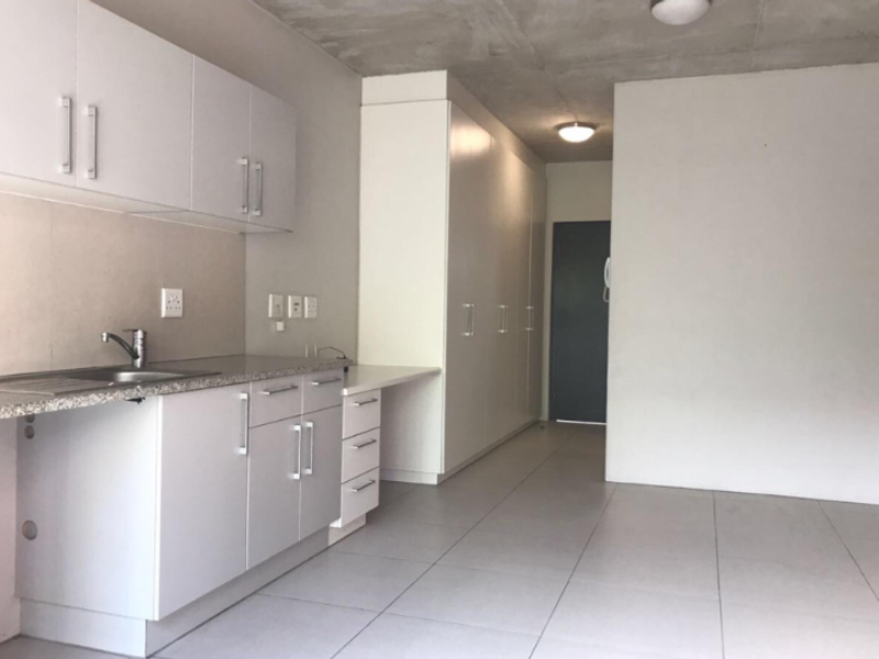 Modern kitchen featuring white built-in cabinetry, stone-look countertops, stainless steel sink, and tiled flooring, set against an industrial-style exposed concrete ceiling.