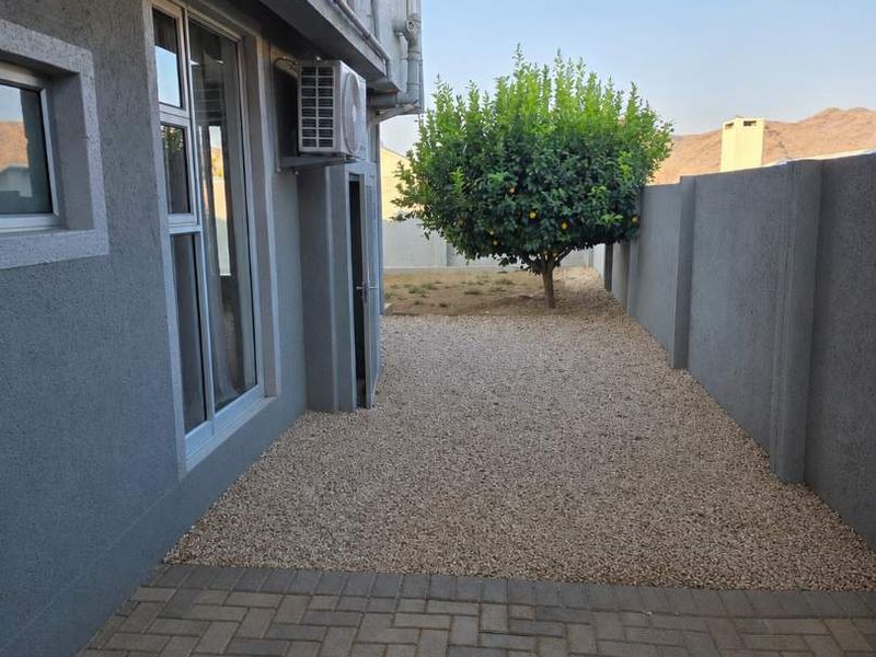 A neat rear exterior area featuring a paved patio, gravel garden, boundary wall, and an installed air conditioning unit.
