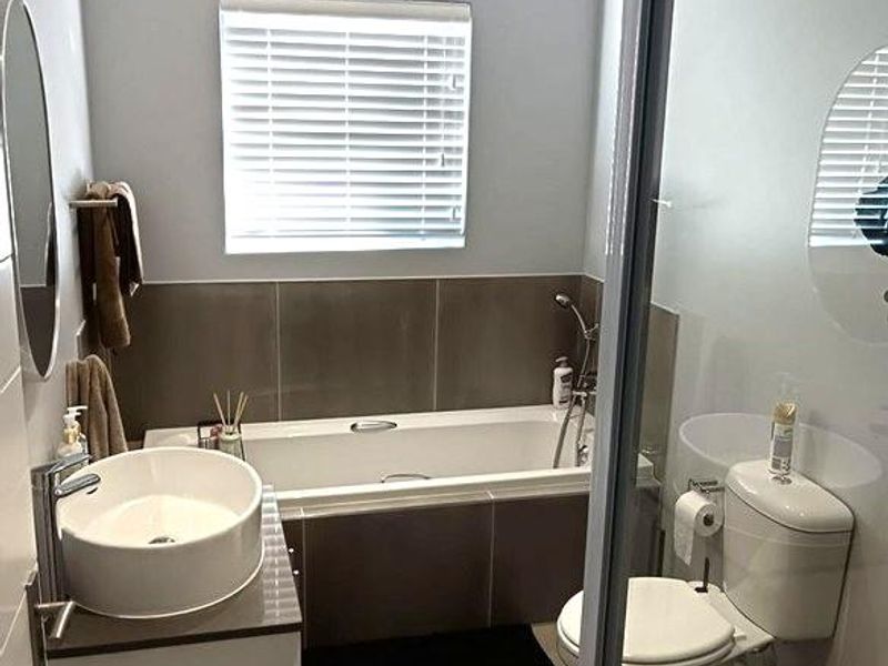 A modern bathroom featuring a built-in bathtub, wall-mounted vanity with vessel sink, toilet, and a separate shower enclosure with neutral tiling.