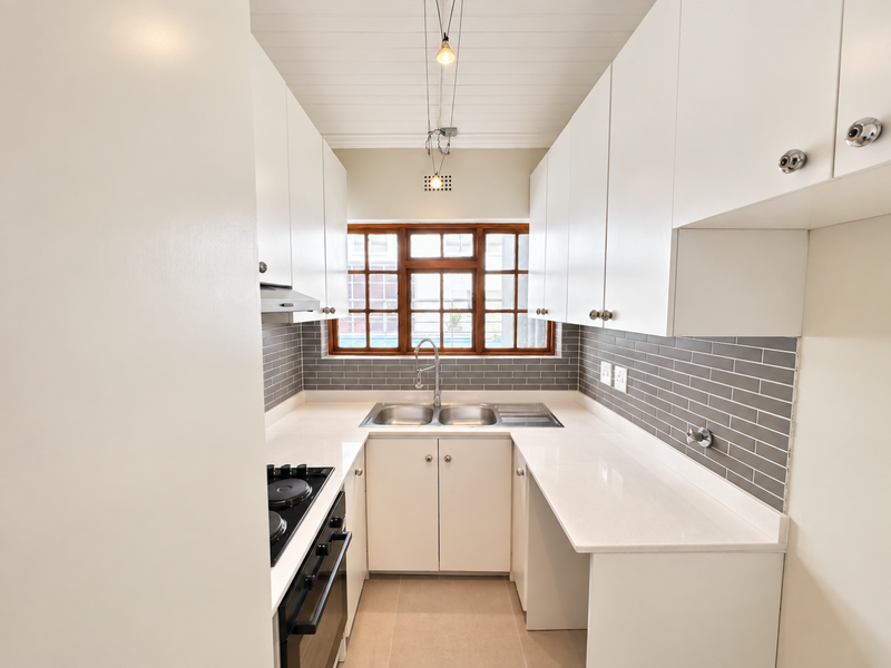 A clean, modern galley-style kitchen featuring white cabinetry, quartz countertops, grey subway tile backsplash, and integrated stainless steel appliances.