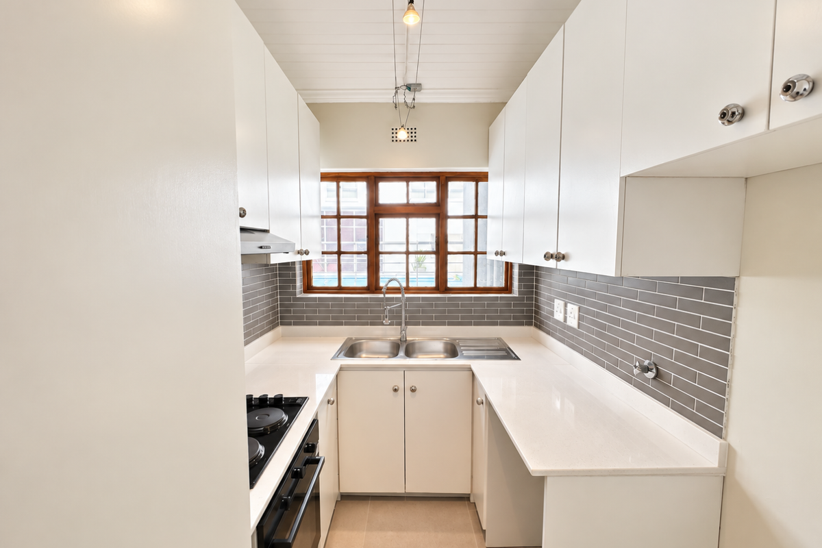 A clean, modern galley-style kitchen featuring white cabinetry, quartz countertops, grey subway tile backsplash, and integrated stainless steel appliances.