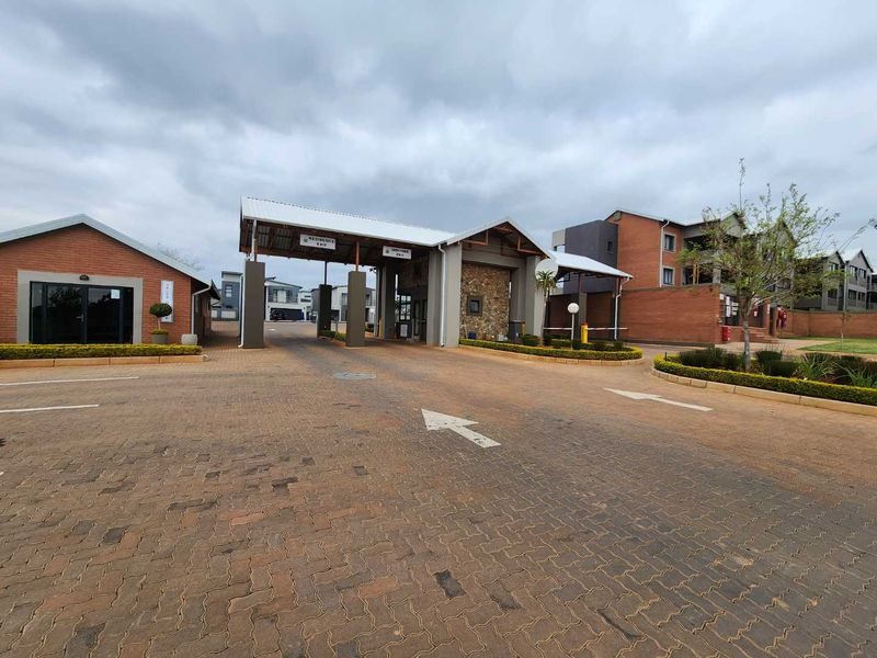 The main entrance and security gatehouse of the apartment complex, featuring brick construction, stone accents, and a paved driveway.