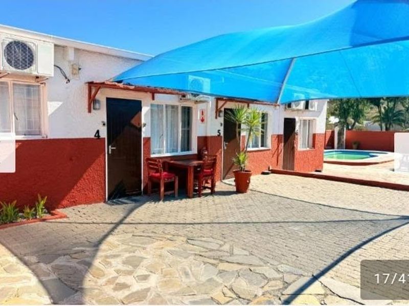 A paved outdoor patio area featuring a large blue shade sail, wall-mounted air conditioning units, and direct access to the building units.