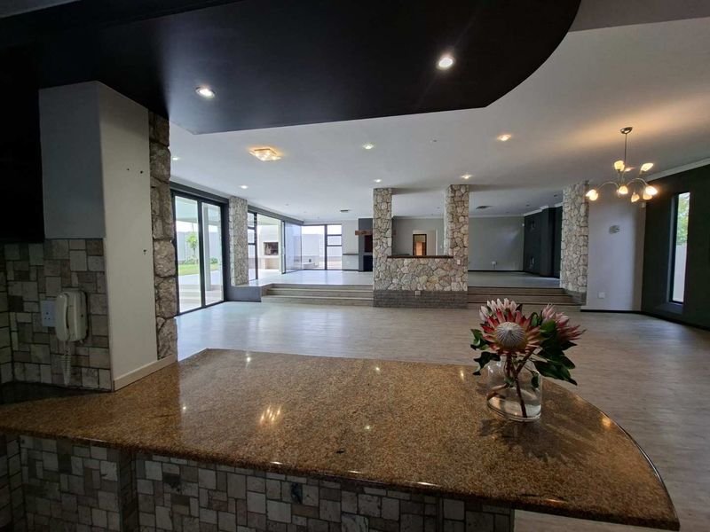 Spacious open-plan living area featuring stone-clad pillars, granite breakfast bar, recessed lighting, and large sliding doors leading to the outdoor space.