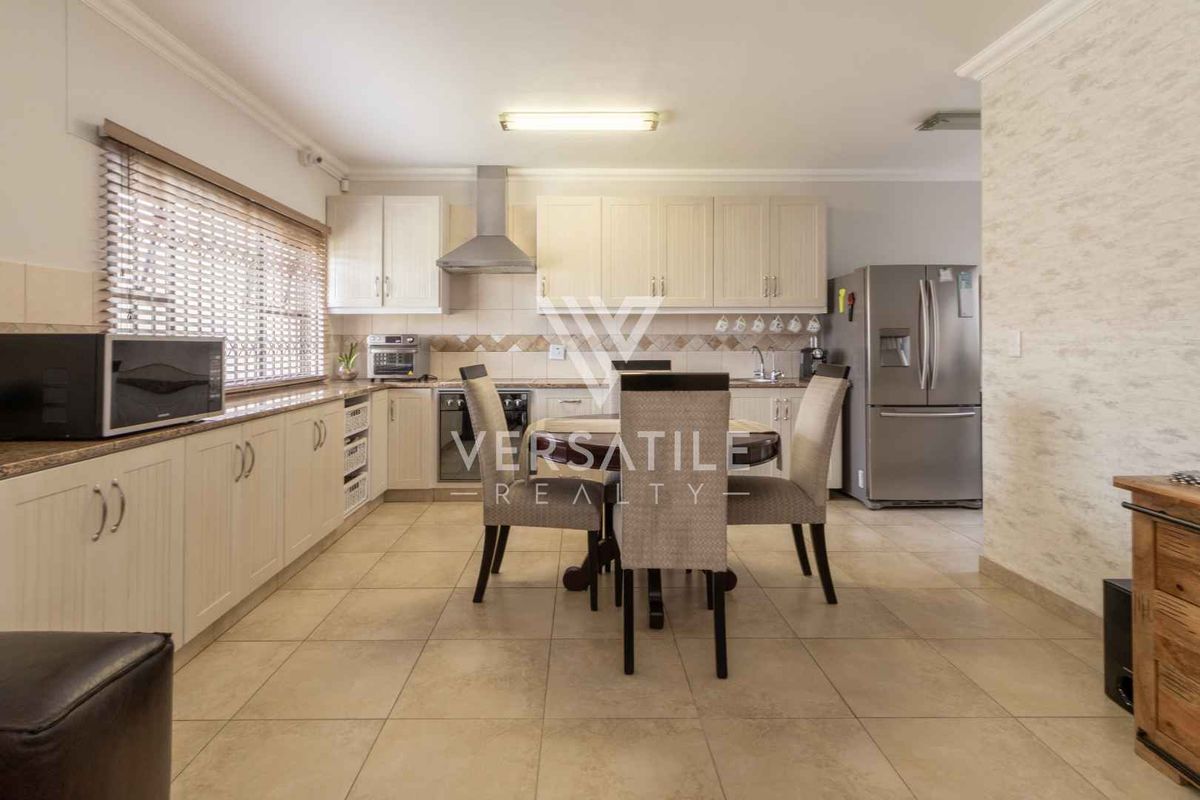 A functional kitchen featuring light-toned cabinetry, tiled backsplash, stainless steel extractor fan, and tiled flooring, offering a practical layout for daily meal preparation.