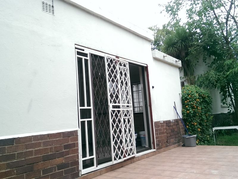 Rear exterior view of the office building featuring a tiled patio, sliding glass door with security gate, and brick facade detailing.