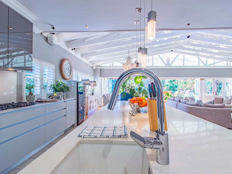 A modern open-plan kitchen featuring a large stone island, sleek cabinetry, and exposed timber rafters, seamlessly flowing into the adjacent living area.
