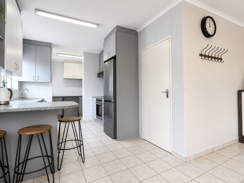 A functional kitchen featuring grey cabinetry, laminate countertops, tiled flooring, and a breakfast bar area, providing a clean and practical workspace.