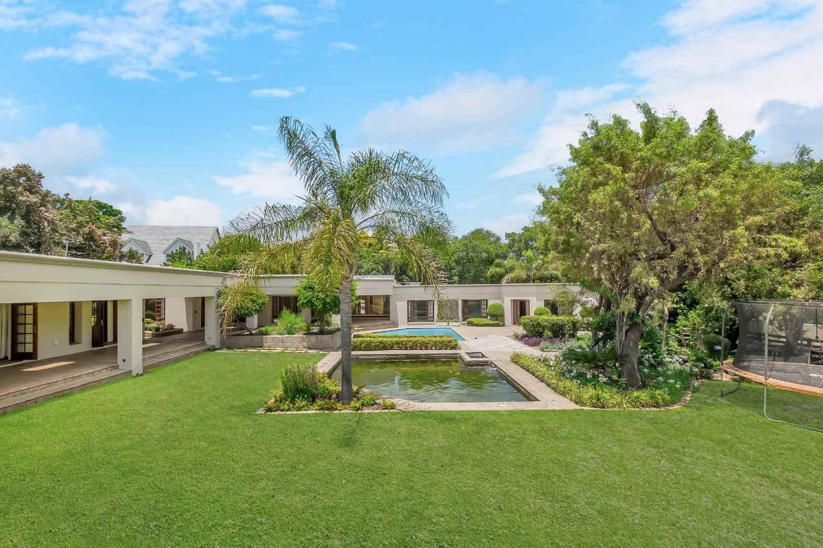Spacious rear garden featuring a swimming pool, a decorative koi pond, a covered patio area, and mature landscaping.