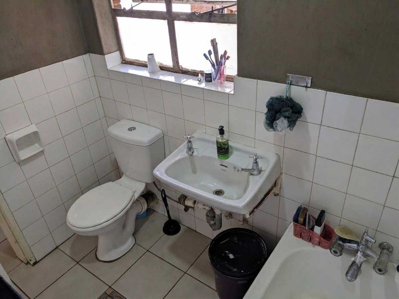 A compact bathroom featuring a standard toilet, wall-mounted basin, and bathtub with tiled finishes, requiring cosmetic updates and maintenance to the plumbing and wall surfaces.