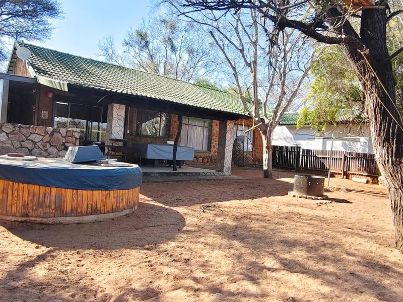 Rear view of the house featuring a covered patio, stone cladding, and a spacious garden area with a built-in fire pit.