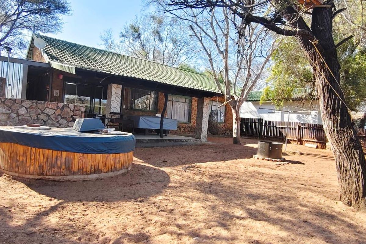 Rear view of the house featuring a covered patio, stone cladding, and a spacious garden area with a built-in fire pit.