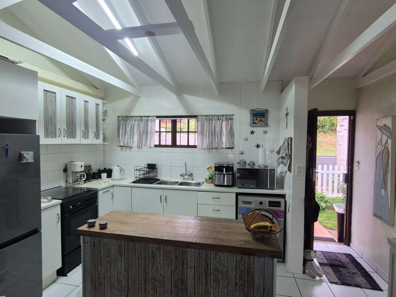 A functional kitchen featuring white cabinetry, tiled splashbacks, exposed ceiling rafters, and a central island, with direct access to the rear exterior.