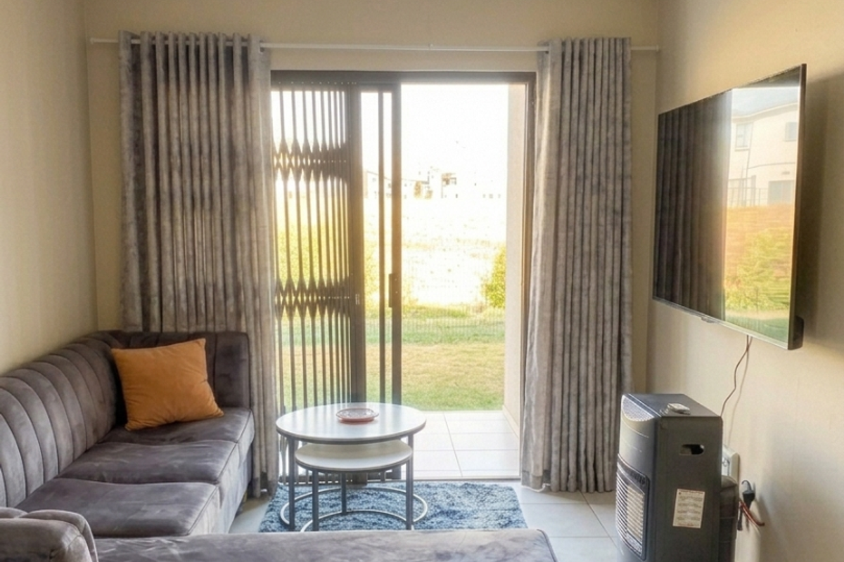 A living room featuring tiled floors and a sliding glass door with a security gate, providing direct access to an outdoor area.