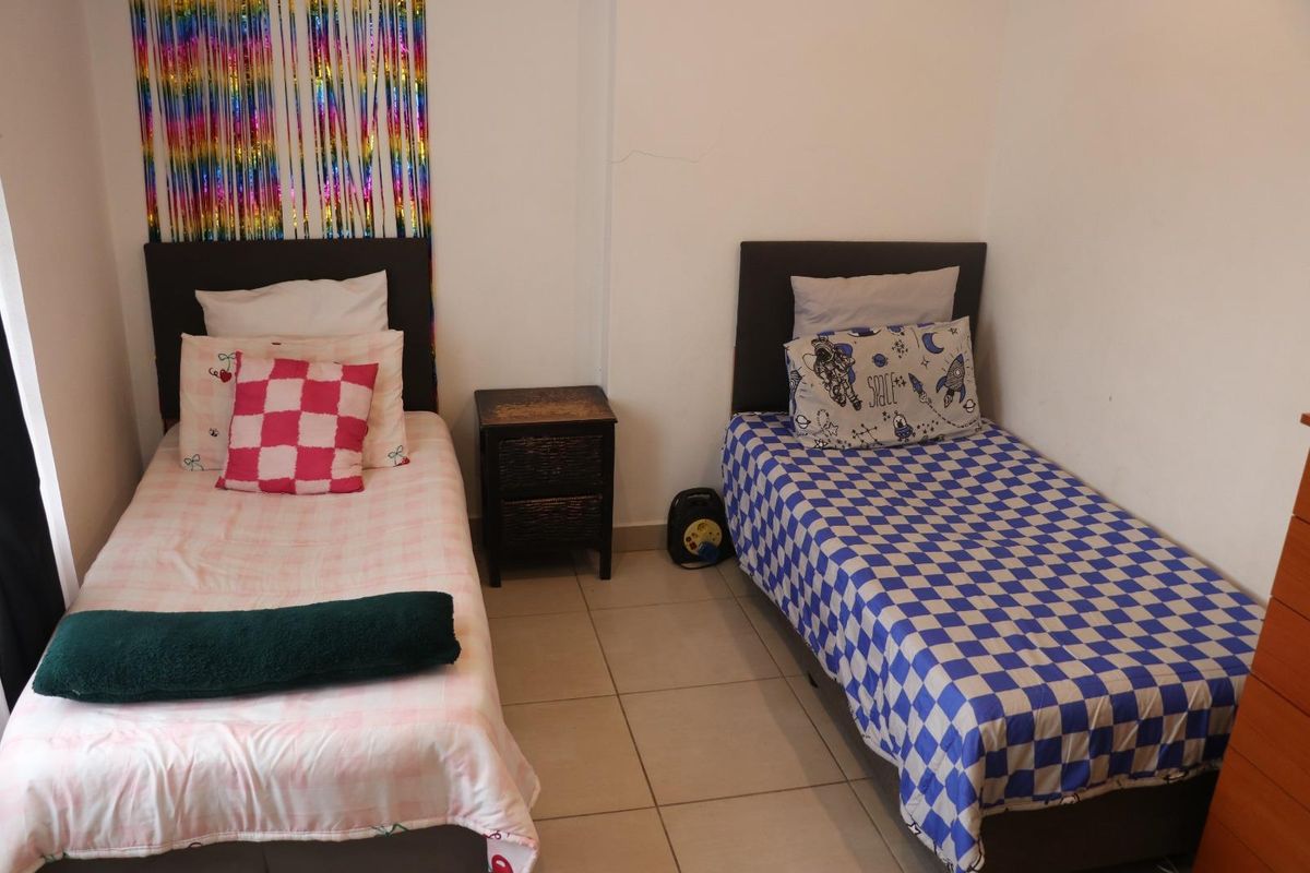 A bedroom featuring tiled flooring and neutral walls, currently configured with two single beds.