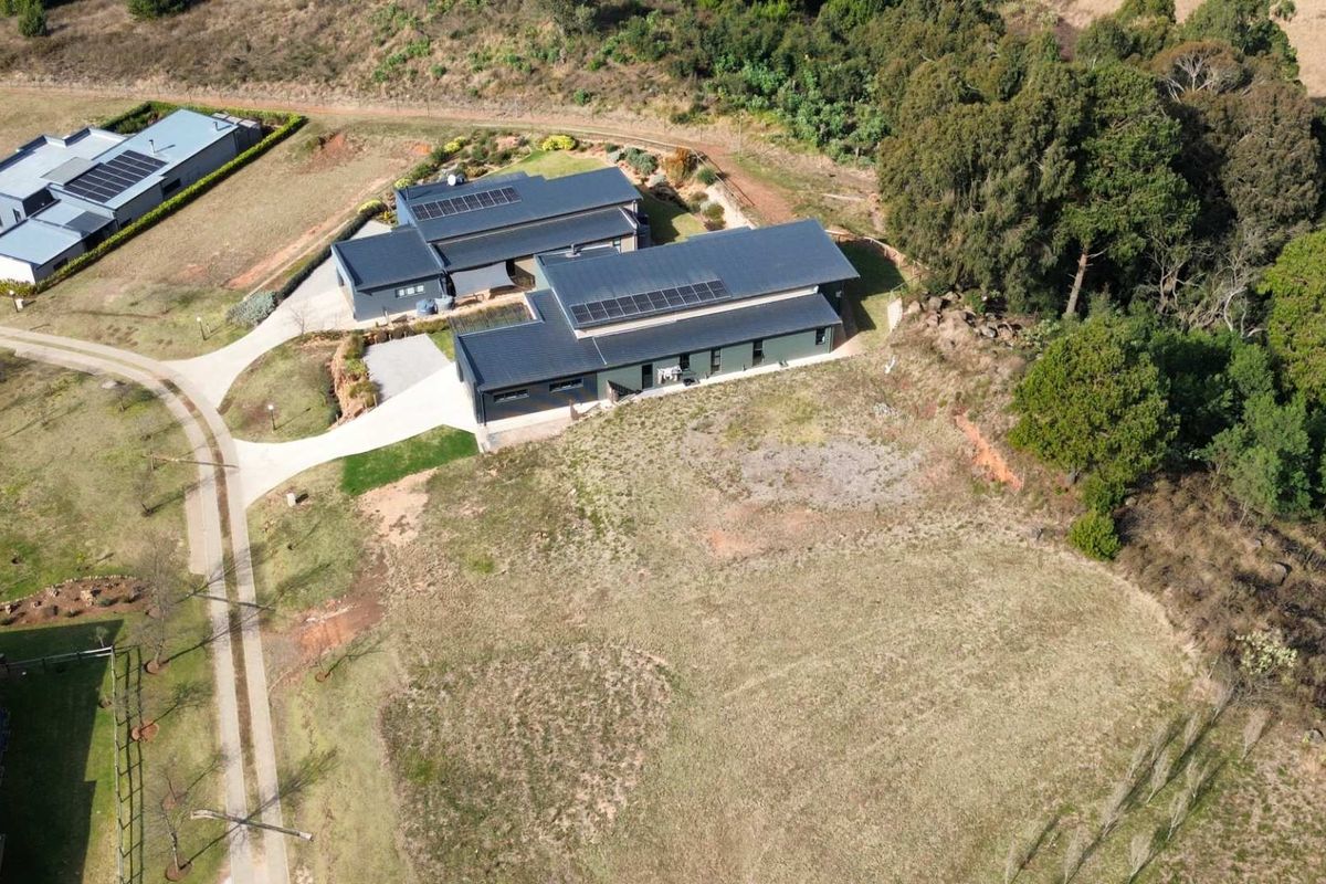 Aerial view of a modern residential property featuring a large dwelling with solar panels, paved driveway, and surrounding landscaped grounds.