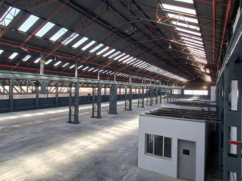 Expansive industrial warehouse space featuring high ceilings with exposed steel trusses, abundant natural light from skylights, and an integrated internal office structure.