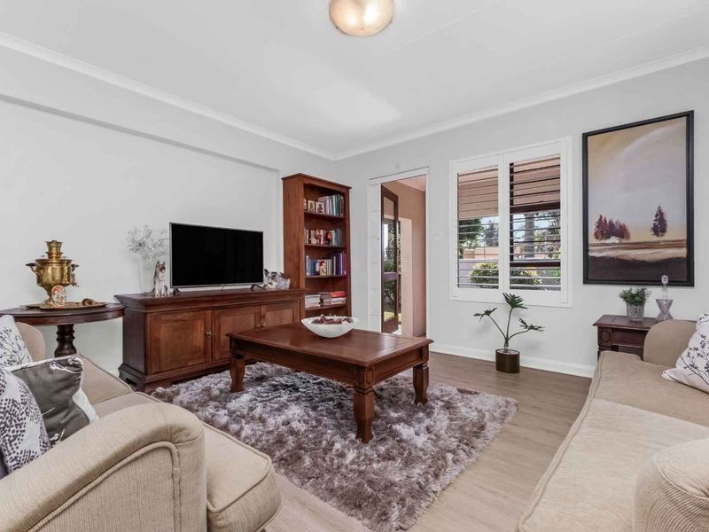 A well-maintained living room featuring laminate flooring, plantation shutters, and neutral wall finishes, providing a comfortable and inviting space.
