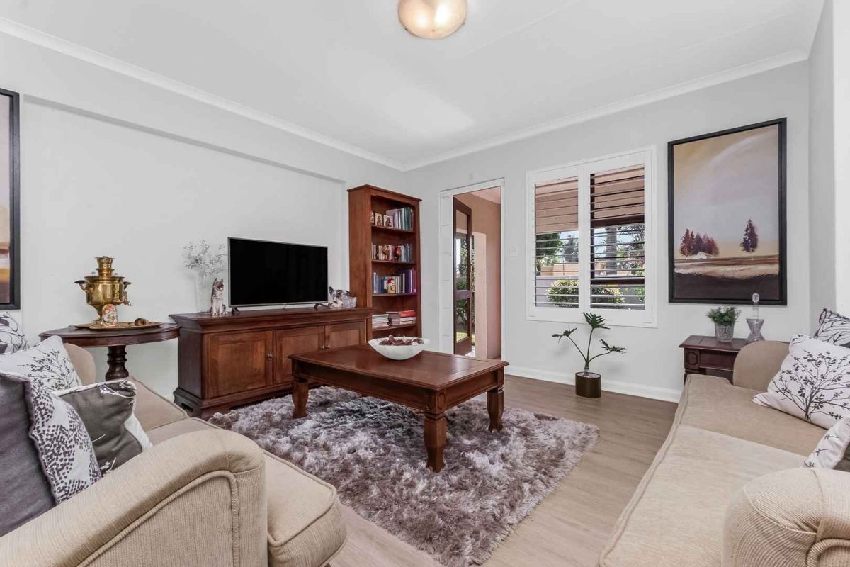 A well-maintained living room featuring laminate flooring, plantation shutters, and neutral wall finishes, providing a comfortable and inviting space.