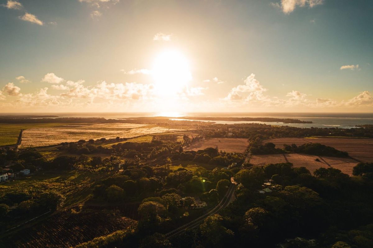 An expansive aerial view of the surrounding landscape, featuring lush greenery, agricultural fields, and a distant coastline at sunset.