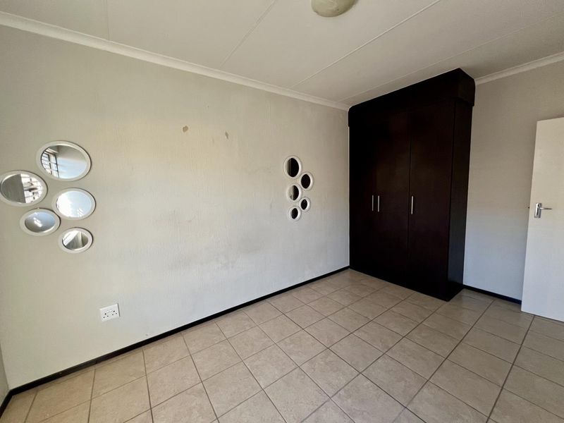 An empty bedroom featuring tiled flooring and a dark built-in wardrobe, requiring minor cosmetic attention to the wall finishes.