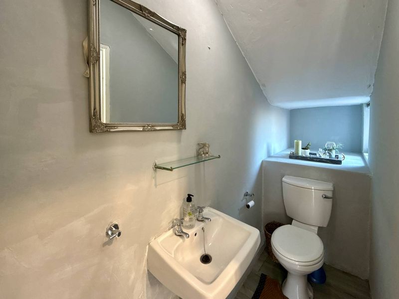 Compact bathroom featuring a wall-mounted basin, toilet, and glass shelving under a sloped ceiling, requiring cosmetic updates to finishes.