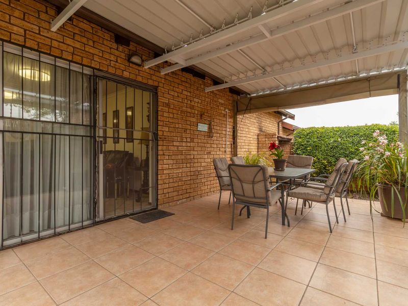 A covered patio area featuring tiled flooring, brick wall construction, and a sliding glass door with security gate access to the interior.