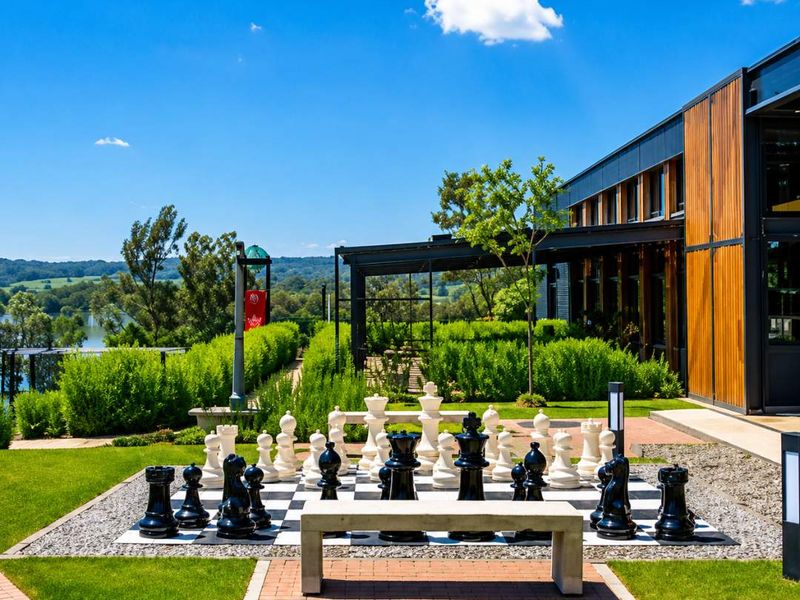 A beautifully landscaped garden area featuring a large outdoor chess set, stone bench, and modern timber-clad building exterior with scenic views.