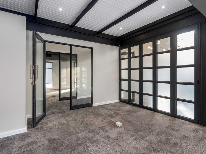Modern office space featuring high-quality glass partitions, exposed ceiling beams, recessed lighting, and neutral carpeting, offering a professional and bright work environment.